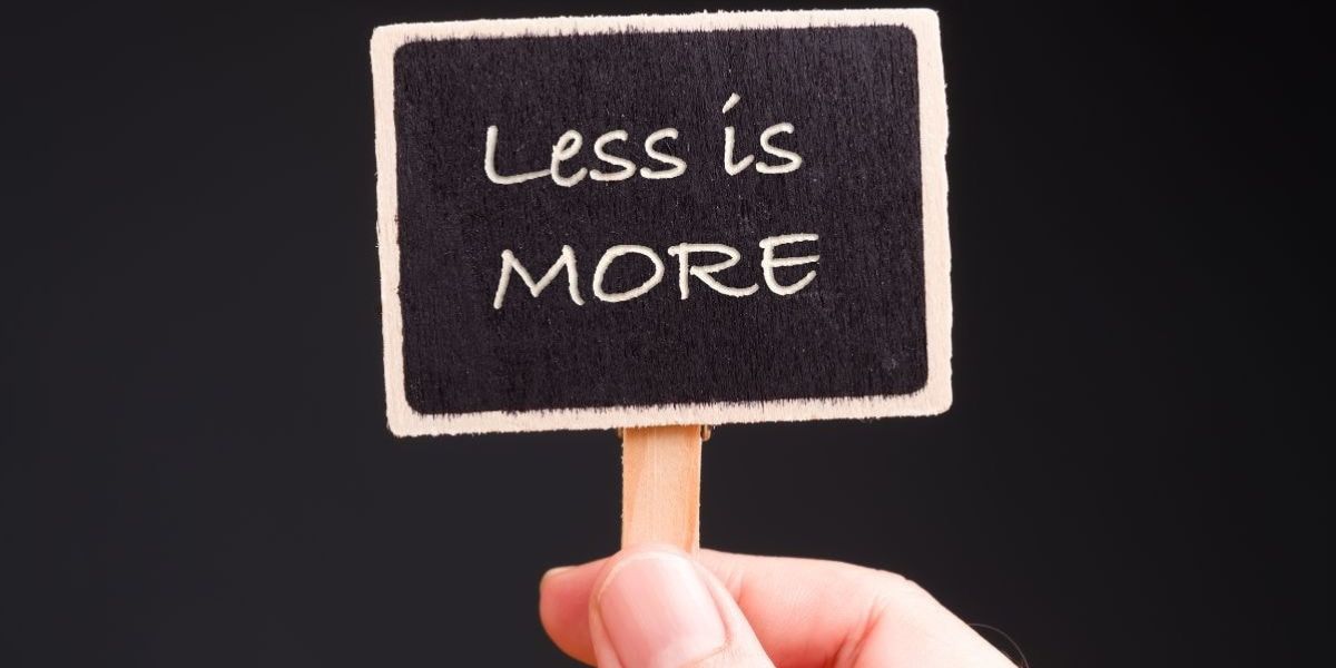 Hand holding a small sign that reads “Less is more,” representing how fewer management layers can lead to greater efficiency and higher mortgage broker compensation.