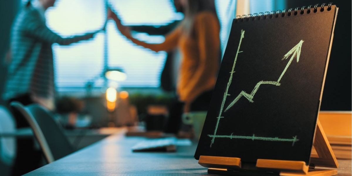 A chalkboard shows a rising growth chart with two people high-fiving in the background, symbolizing the success and increased earnings of mortgage brokers working under a producing branch manager.